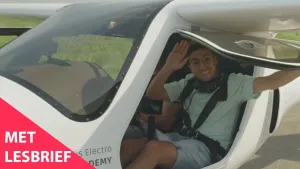 Een foto van de presentator. Hij zit in een klein elektrisch vliegtuigje en houdt de deur omhoog. Hij zwaait naar de kijker. Linksonder in beeld staat de tekst "Met lesbrief".