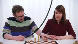 Een foto van Diederik en Ionica achter een witte tafel. Op de tafel staat een schaakbord met bruine en witte vakjes. Op vier vakjes liggen bruine suikerklontjes opgestapeld, van links naar rechts één klontje, twee klontjes, vier klontjes en acht klontjes.