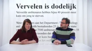 Een foto van Diederik en Ionica achter een witte tafel. Voor hen staat een zwarte tekst. De kop van de tekst is "Vervelen is dodelijk" en de eerste regel is "Verveelde ambtenaren hebben bijna 40 procent meer kans om jong te sterven".