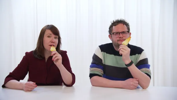 Een foto van Diederik en Ionica achter een witte tafel. Ze hebben allebei een waterijsje in hun linkerhand. Het waterijsje is van de soort raket, die de vorm van een raket heeft en onderaan geel is, oranje in het midden en de punt bovenop rood.