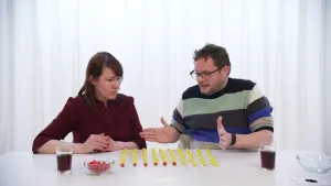 Een foto van Diederik en Ionica achter een witte tafel. Op de tafel staan twee glazen cola en liggen 100 balletjes. Zes balletjes zijn rood en 94 geel, dat betekent rood 6% en geel 94% kans. In een glazen schaaltje ervoor liggen meer rode balletjes. 