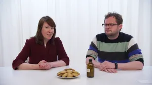 Een foto van Diederik en Ionica achter een witte tafel. Op tafel staat een wit bord met ronde, lichtbruine koekjes. Ook staat er een bruin flesje met een witte, op de foto niet leesbare, sticker erop. In de uitzending is "medicijn" op de sticker te lezen.