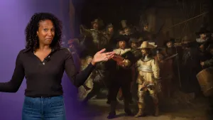 Een foto van een presentator naast een foto van het schilderij "De Nachtwacht" van Rembrandt van Rijn. Twee mannen vooraan zijn goed te zien: één in een zwart kostuum met rode band om zijn schouder, één in een lichtbruin kostuum die een speer vastheeft.