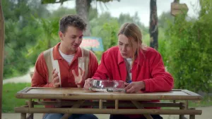 Een foto van presentatoren Emma en Jurre die aan een tafel zitten en naar een glazen schaal kijken waar bloedzuigers in zitten. 