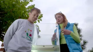Een foto van presentatoren Jurre en Emma die boven een bak met water staan en erin kijken. Er zitten zwemwantsen in de bak. Een zwemwants is een insect die in het water leeft.