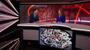 Een foto van een halfronde tafel waar rechts een presentator achter zit en links hoogleraar Reinout Wiers. Voor de tafel hangt een beeldscherm met sigarettenpeuken die in een rond gat op elkaar liggen. De peuken zijn wit met een bruin stuk aan één kant.