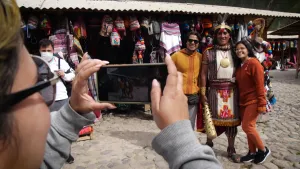 Een foto van maïsboer Adolfo in Peru. Hij lijkt op een Inca strijder en poseert in de kleren die zo iemand vroeger droeg. Hij gaat op de foto samen met twee toeristen. Op de achtergrond zie je een winkel. 