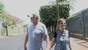 Een foto van een oudere man en vrouw. Ze lopen hand in hand op straat. De man heeft een petje op. De vrouw glimlacht. 