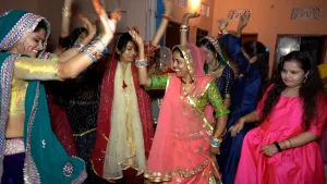 Een foto van een groep Indiase vrouwen die in een kamer aan het dansen zijn. Ze steken hun armen omhoog en hebben allemaal kleurrijke kleren aan. 