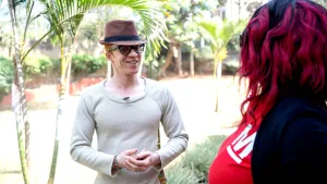 Een foto van een Afrikaanse man met albinisme. Albinisme is een aandoening waardoor mensen een hele witte huid hebben en slechter kunnen zien. De man heeft een hoed op en is in gesprek met een Afrikaanse vrouw. 