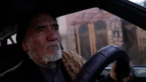 Een foto van een man die achter het stuur zit van een auto en aan het rijden is.