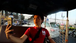 Een foto van een jongen die achterin een kleine auto zit en met een telefoon een foto van zichzelf maakt.