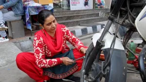 Een foto van een Indiase vrouw die bezig is met het repareren van een motorfiets.