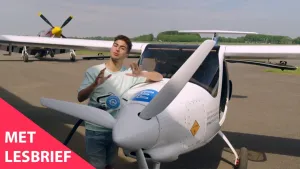 Een foto van Nizar in zomerse kleding die leunt tegen de zijkant van een wit elektrisch vliegtuig waar twee mensen inpassen. Het heeft een propeller met drie wieken en twee brede vleugels. Linksonder staat in een rode driehoek "Met Lesbrief".