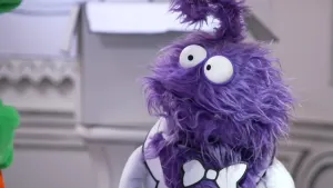 Een foto van een paarse pop die naar een groene pop kijkt waarvan een klein stukje te zien is aan de linkerkant.