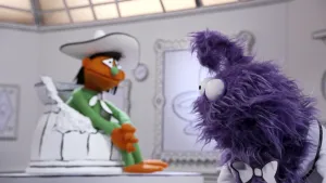 Een foto van een oranje pop die in een gebroken pot zit in het museum van gewone dingen. Op de voorgrond is het hoofd te zien van een paarse pop.