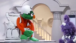 Een foto van een groene pop die in het museum van gewone dingen in een gebroken pot zit en naar een paarse pop kijkt.