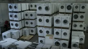 Een foto van een magazijn vol met wasmachines. Ze zijn op elkaar gestapeld.