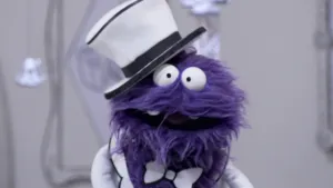 Een foto van een paarse pop die in de camera kijkt terwijl de pop in het museum van gewone dingen staat.