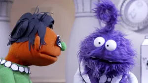 Een foto van een blauwe pop. Dat is de presentator. Tegenover hem staat een oranje pop. Dat is de gast. Zij heet Truus. 