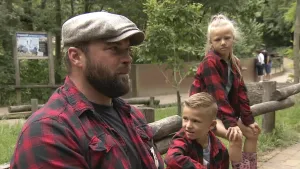 Een foto van boswachter Tim. Hij zit op een bankje in een dierentuin. Naast hem zitten een jongen en een meisje. Ze hebben alle drie een roodzwart-geruit overhemd aan.