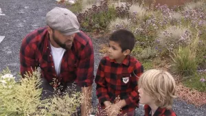 Een foto van boswachter Tim. Naast hem zie je twee kinderen. Ze zijn met elkaar in gesprek. Voor en achter hen zie je allemaal bloemen en planten.