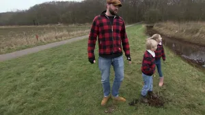 Een foto van boswachter Tim. Naast hem zie je twee kinderen. Ze staan naast een sloot. Ze kijken allemaal in de richting van die sloot. Op de achtergrond zie je een bos.