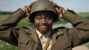 Een foto van presentator Tirsa. Ze staat buiten tussen de weilanden. Ze heeft een legeruniform aan, en een legerhelm op haar hoofd. Ze houdt de helm met beide handen vast en kijkt in de camera.