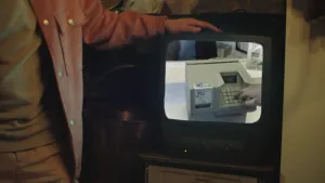 Een foto van een ouderwetse televisie met een beeldbuis vorm, waarin een filmpje te zien is van iemand die zijn of haar pincode intoetst op een ouderwets grijs pinapparaat. De arm van presentator Pascal ligt op de televisie, zijn gezicht is niet te zien.