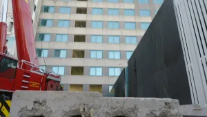 Een foto van een flatgebouw in aanbouw. Op de voorgrond zie je een stuk beton. Links in beeld zie je een bouwkraan.