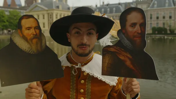 Een foto van presentator Nizar bij de Hofvijver in Den Haag. Hij heeft zestiende-eeuwse kleding aan. Hij houdt twee foto's op een bordje vast. De linkerfoto toont Johan van Oldenbarnevelt. De rechterfoto toont Prins Maurits van Oranje.