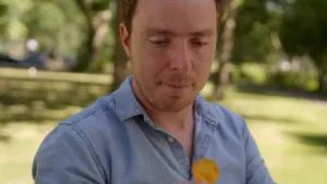 Een foto van een man die buiten staat. Hij heeft iets geels in zijn handen. Het lijkt op een chipje. Hij kijkt ernaar.