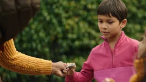 Een foto van jongetje Sammy die wat briefjes geld krijgt van iemand. Van die persoon zie je alleen een arm in beeld. Sammy kijkt naar de briefjes terwijl hij ze aanpakt.