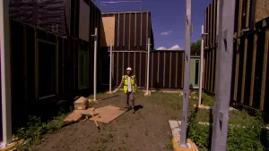 Een foto van presentator Pascal. Hij heeft een helm op en een felgele jas aan. Hij staat tussen een aantal half afgebouwde woningen.