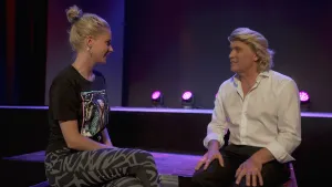 Een foto van presentator Janouk en illusionist Hans Klok. Een illusionist is een soort goochelaar. Ze zitten met elkaar te praten. Op de achtergrond zie je een rij paarse lampen.