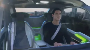 Een foto van een man in een vliegende auto. Hij hoeft niet te sturen en kijkt naar buiten. Op de achtergrond zie je een stad onder hem.