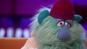 Een foto van het gezicht van een bedroefd kijkende pop die Piet van Tranen heet. De pop draagt een rode muts en witte trui. hij heeft een lichtgroene baard en een grote, lichtblauwe neus. Zijn ogen kijken bedroefd, omdat hij een winterdip heeft. 