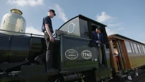 Een foto van Nizar die in de opening staat van de cabine van de machinist in een oude stoomtrein. Hij kijkt naar een medewerker die aan de voorkant van de stoomtrein staat naast het gedeelte met de pijp. Op de trein staat "Nederlandsche Spoorwegen 7742". 