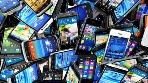 Een foto van tientallen smartphones. Ze liggen dwars door elkaar heen en staan allemaal aan.