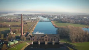 Een foto van een gemaal, gezien vanuit de lucht. Een gemaal is een gebouw om water van een lager naar een hoger niveau te brengen. Verder zie je, naast water, weilanden, bomen en een dorp.