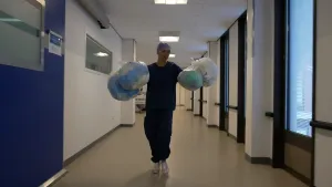 Een foto van presentator Serah die in een ziekenhuis uniform door een gang loopt in het ziekenhuis met zakken afval in beide handen.