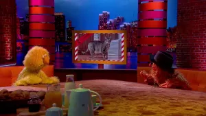 Een foto van twee poppen, dierendetective Davy Blaffer en een presentator naast een scherm met een foto van een gestreepte kat. De presentator zit links met een gele vacht. Davy Blaffer zit rechts en heeft een roodbruine vacht en een zwarte hoed op. 