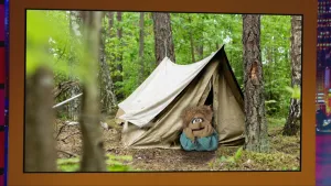 Een foto van een tent in een bos. In de opening van de tent ligt een pop, die naar de camera kijkt. Ze leunt met haar hoofd op haar handen.
