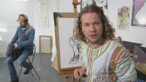 Een foto van presentator Pascal die achter een schilder standaard zit met daarop een tekening van een man die middenin de kamer op een stoel zit met geluidsapparatuur in zijn handen en een koptelefoon op.