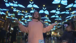 Een foto van presentator Pascal die buiten in de donker onder een net staat van gemaakte lichtgevende vlinders.