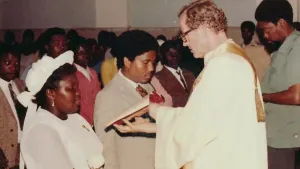 Een foto van een missionaris die een opengeslagen boek aan een zwarte vrouw toont. Het is onderdeel van een kerkdienst in Afrika.