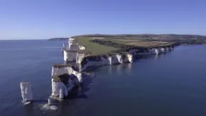 Een foto van de witte krijtrotsen langs de zuidkust van het Verenigd Koninkrijk. Op de rotsen zijn groen gras en groene struiken te zien. Het water om de rotsen heen is donkerblauw van kleur.