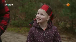 Een foto van een jong meisje in een bos. Ze kijkt naar een man die naast haar staat. Het meisje heeft een sjaal om haar hoofd gebonden.