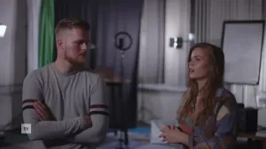 Een foto van een man en een vrouw die in een kamer zitten. Links zit de man. Hij heeft zijn armen over elkaar en luistert naar de vrouw. Rechts zit de vrouw. Ze is iets aan het vertellen aan die man.