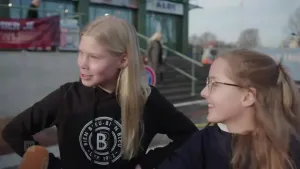 Een foto van twee meisjes van een jaar of dertien die worden geïnterviewd op straat. Op de achtergrond zie je winkels.